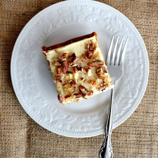 square slice of cake with cream cheese frosting and chopped pecans