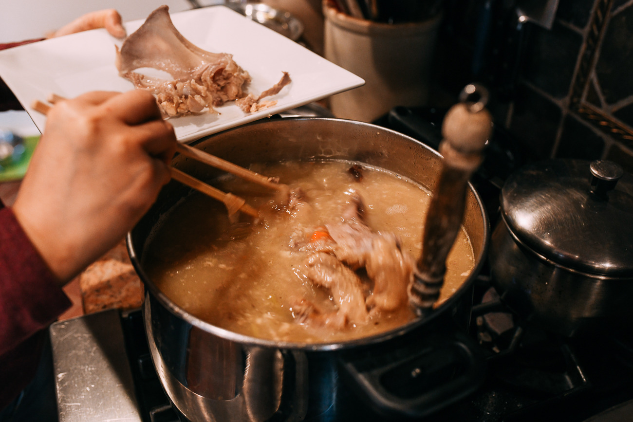Removing turkey carcass bones from pot of congee
