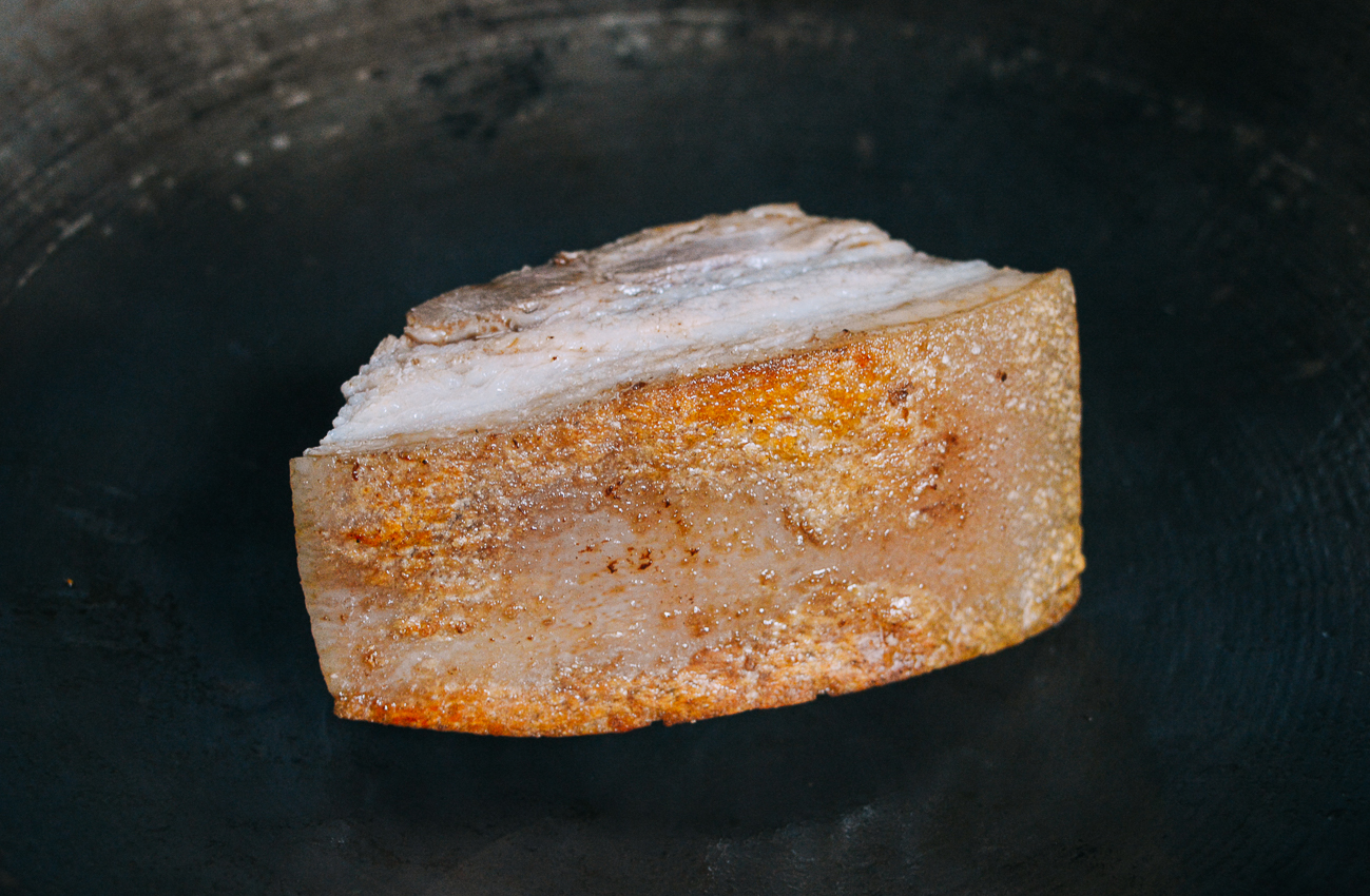 searing chunk of pork belly in wok with crispy skin