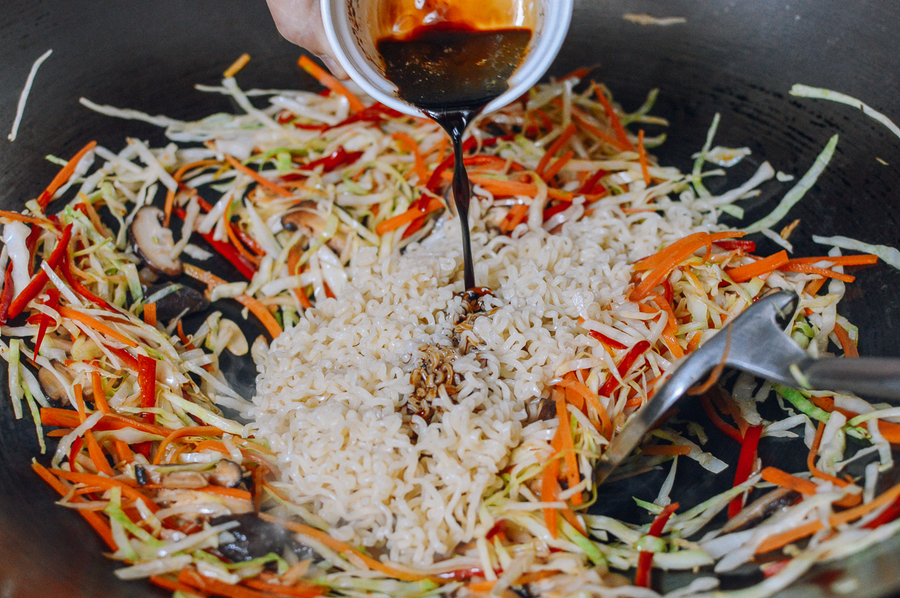 adding sauce to ramen noodles in wok