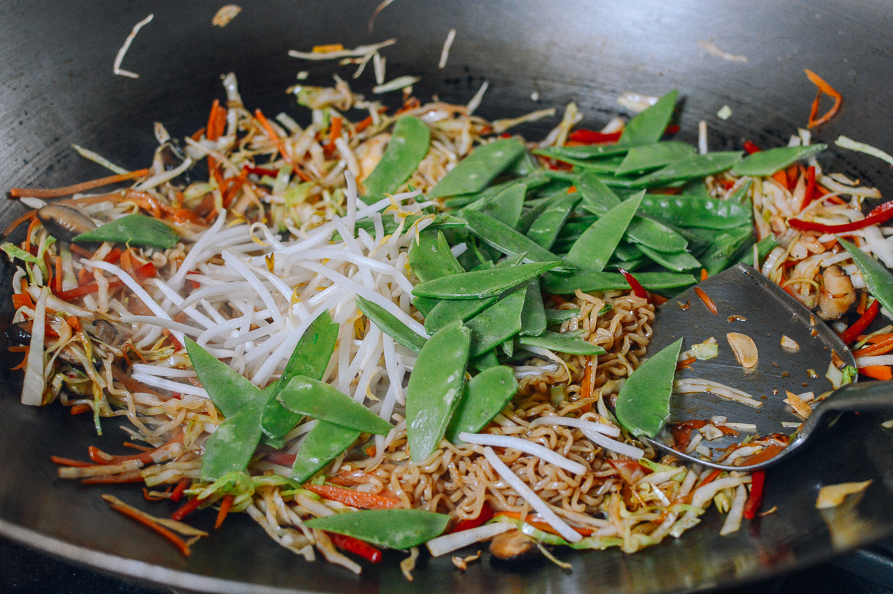 adding bean sprouts and snap peas to noodles and vegetables