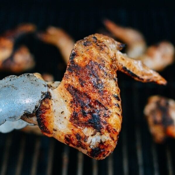 Tongs holding grilled chicken wing
