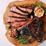 Sliced ribeye steak with roasted garlic on cutting board