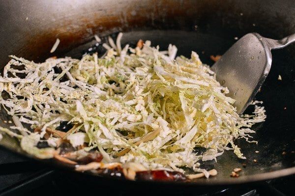 Adding shredded cabbage to wok, by thewoksoflife.com