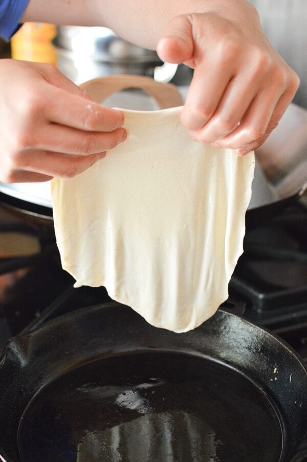 placing thin dough in pan for Jidan Bing, by thewoksoflife.com