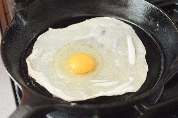 raw egg on thin dough in pan for Jidan Bing, by thewoksoflife.com