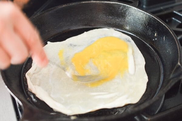 stirring raw egg on thin dough in pan for Jidan Bing, by thewoksoflife.com