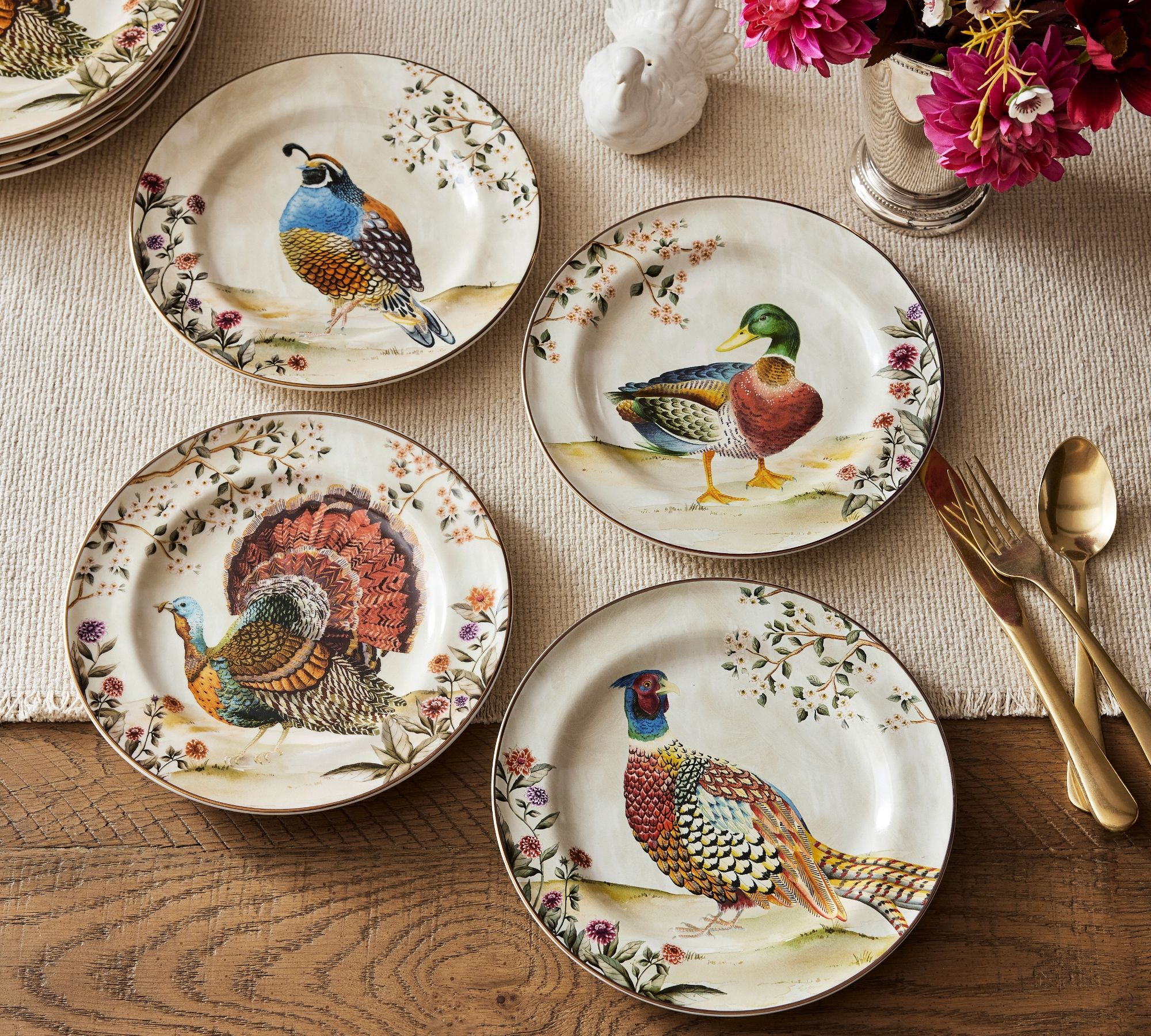 painted plates with quail, mallard, partridge, and turkey on each with a rustic tablesetting and gold flatware 