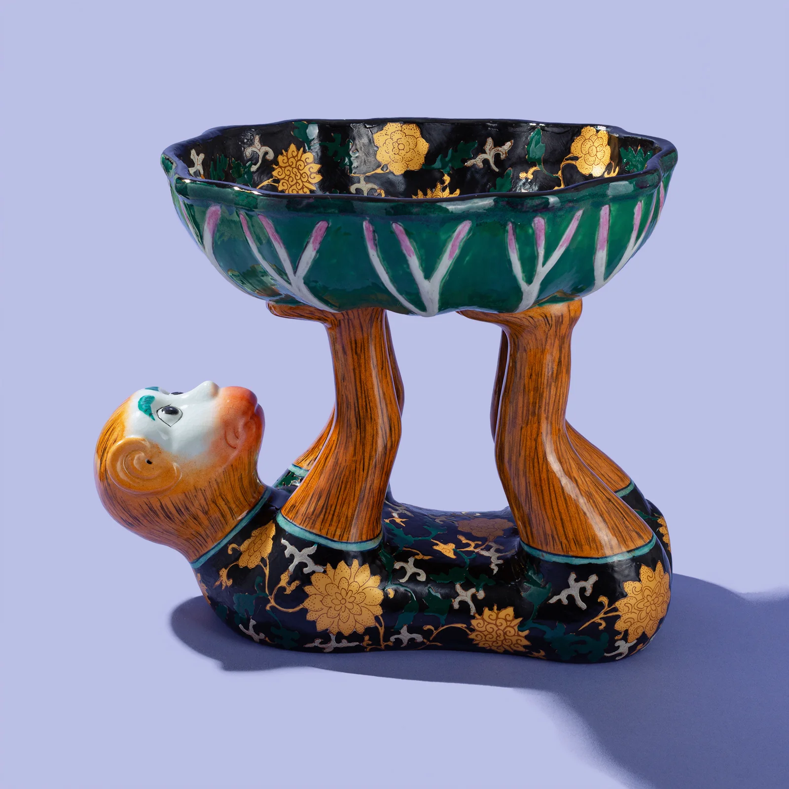 porcelain monkey holding up a lotus leaf bowl painted in black, gold, and teal 