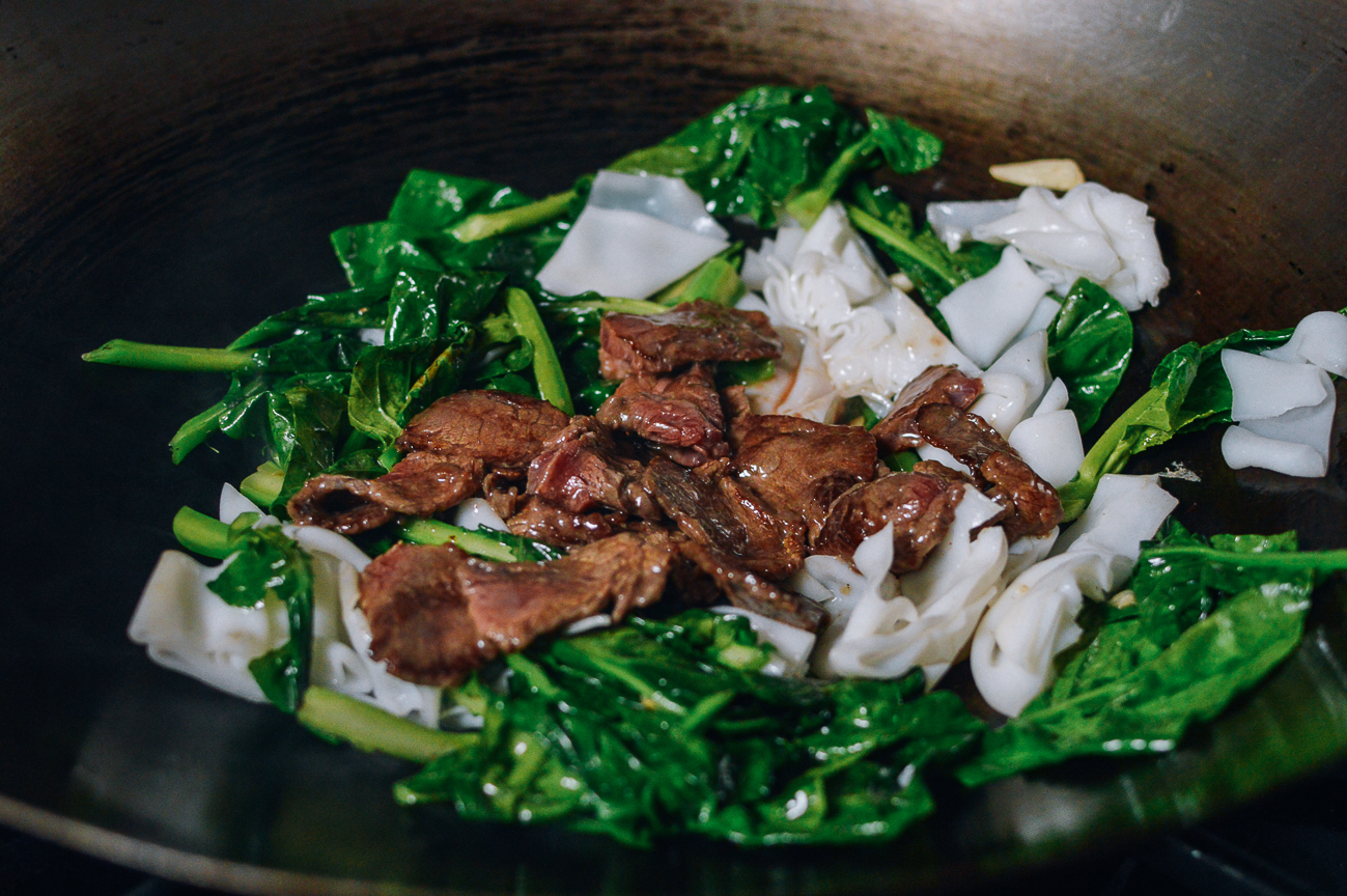 Adding beef to Chinese broccoli and rice noodles in wok