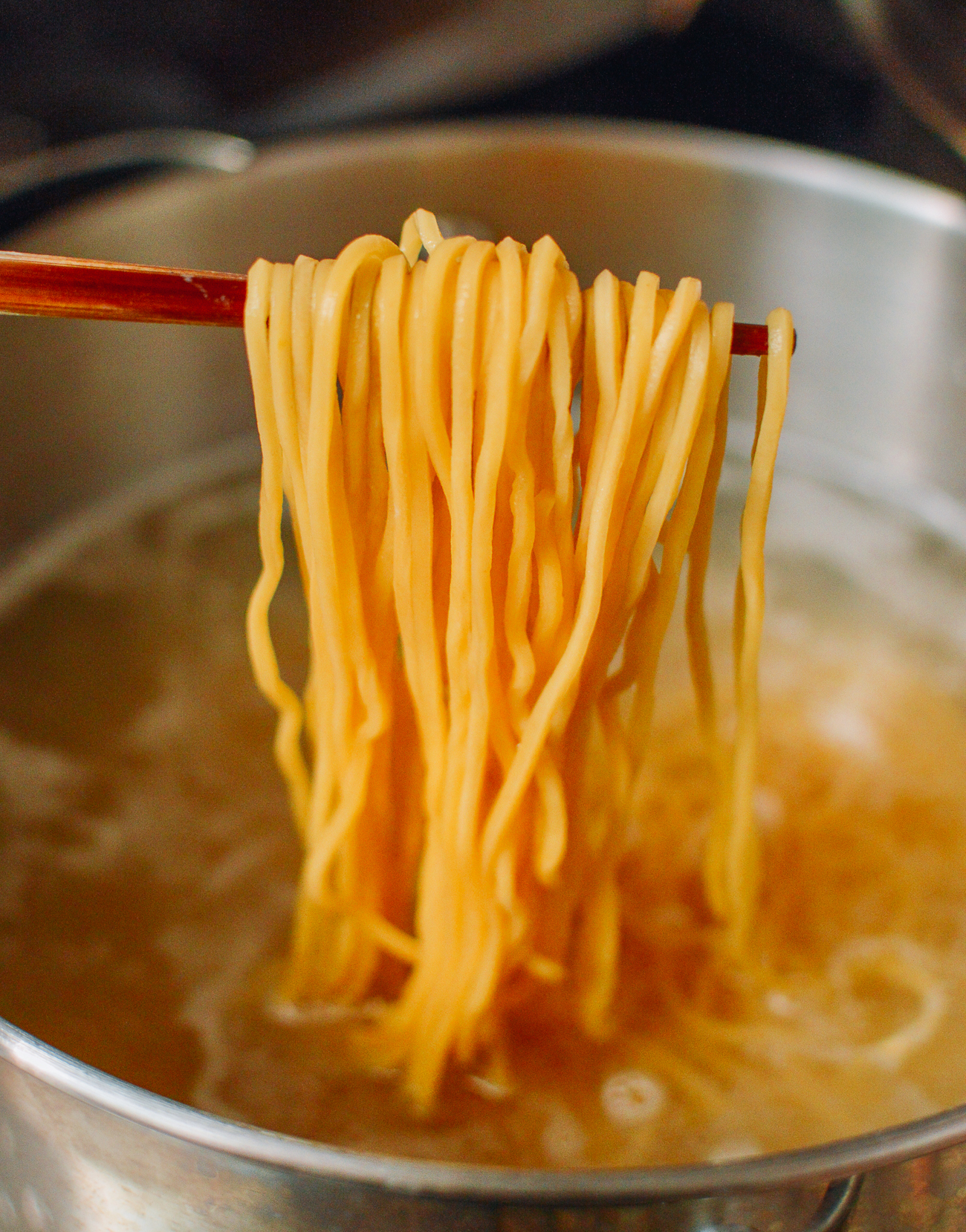 pulling egg noodles out of boiling water with chopsticks