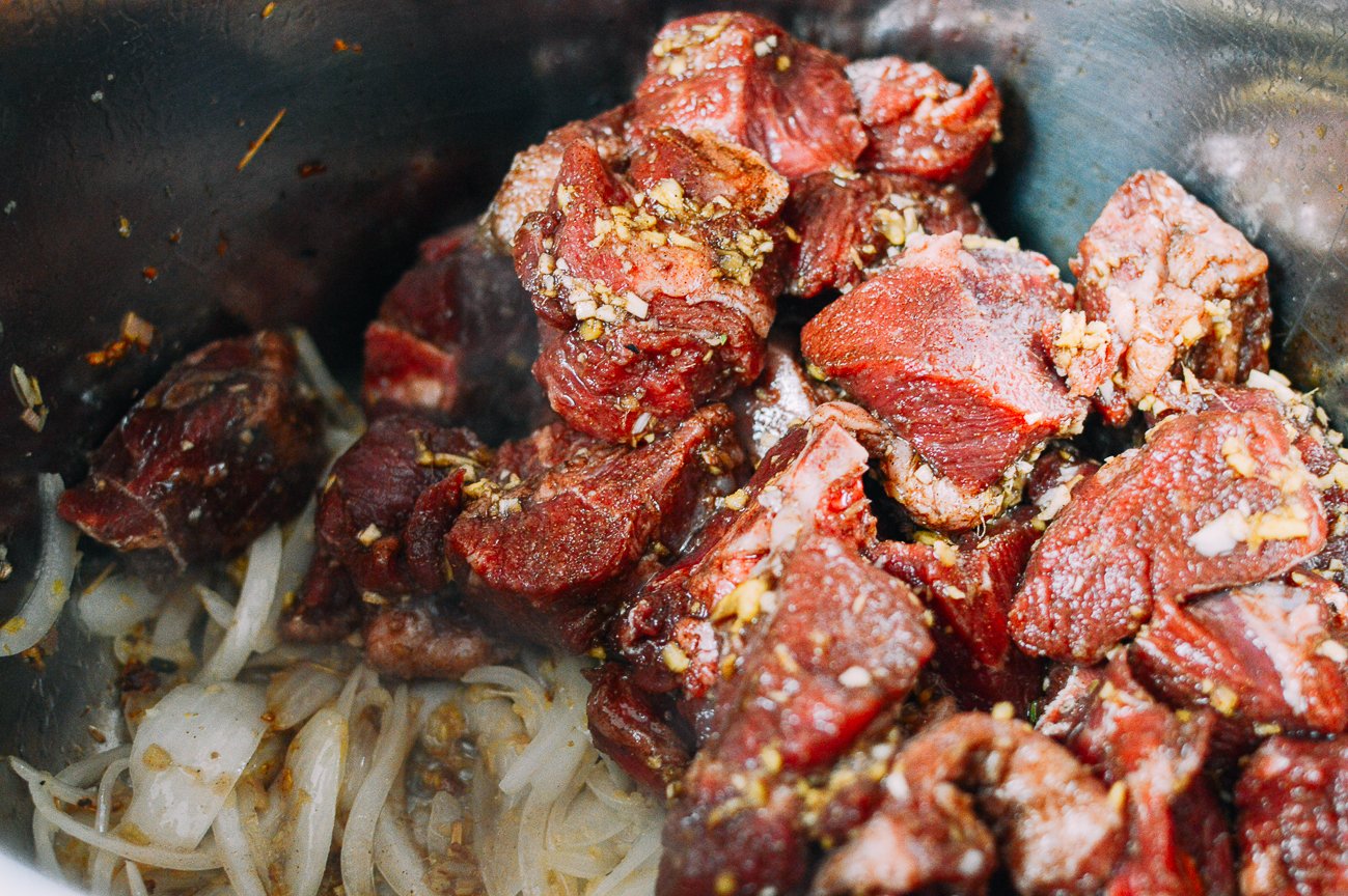 Adding marinated beef chunks to lemongrass and onions