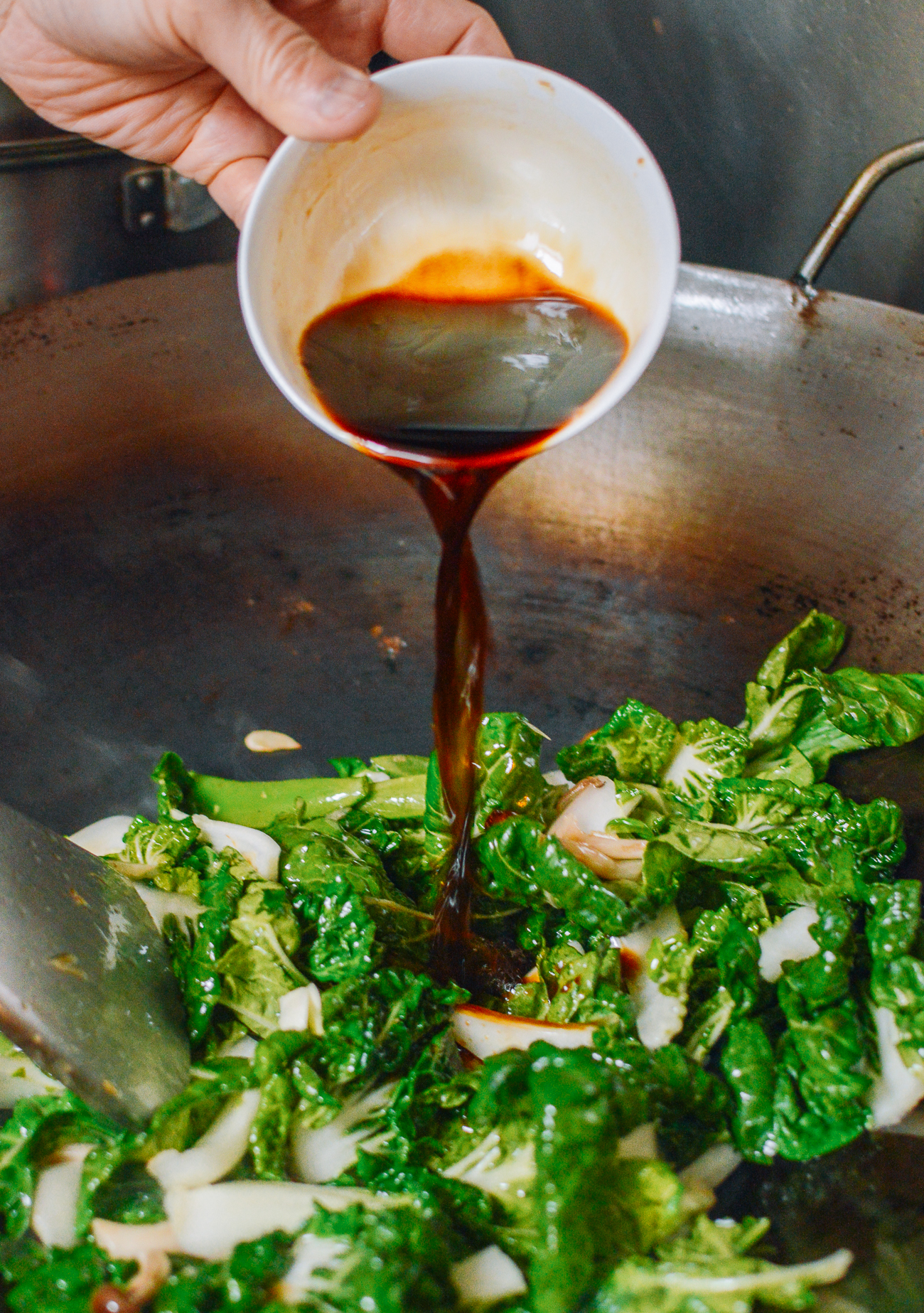 adding sauce to green vegetables in wok