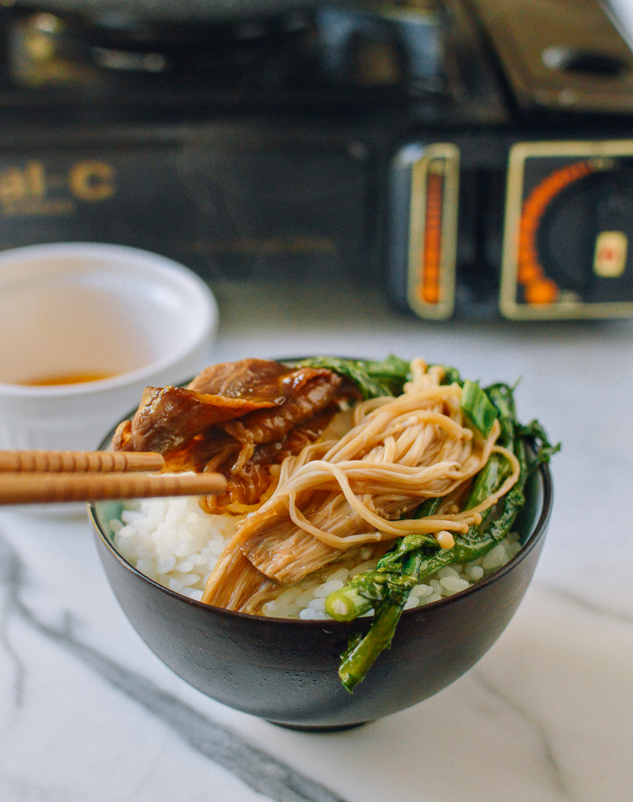 beef, enoki mushrooms, and chrysanthemum leaves on bowl of rice