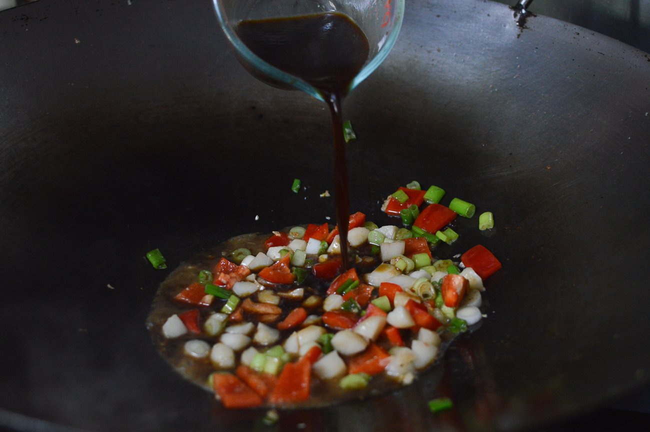 Pouring sauce ingredients into wok with vegetables