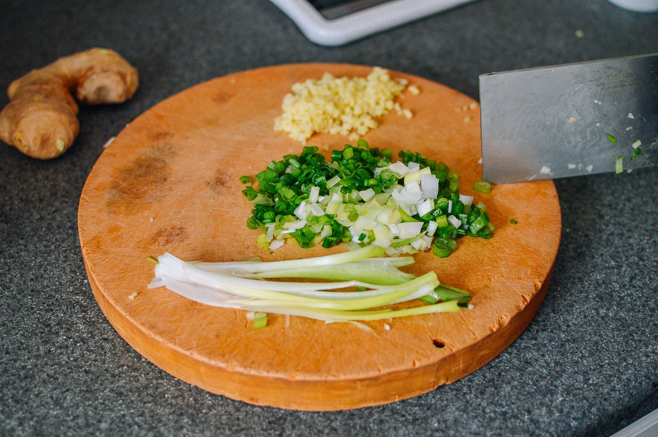 chopped scallions and ginger on small round cutting board