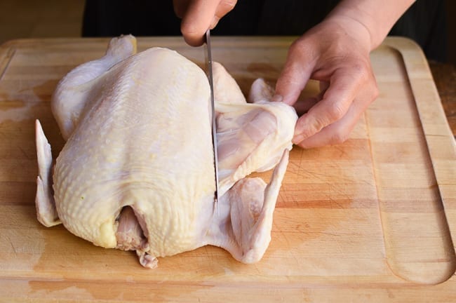 Slicing through skin between drumstick and rest of chicken