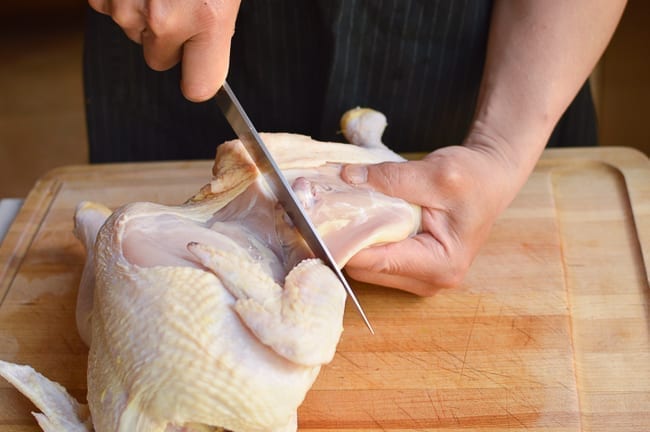 Using knife to separate chicken leg quarter from the rest of the chicken