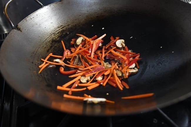 Adding carrots, peppers, and mushrooms to garlic in wok, thewoksoflife.com