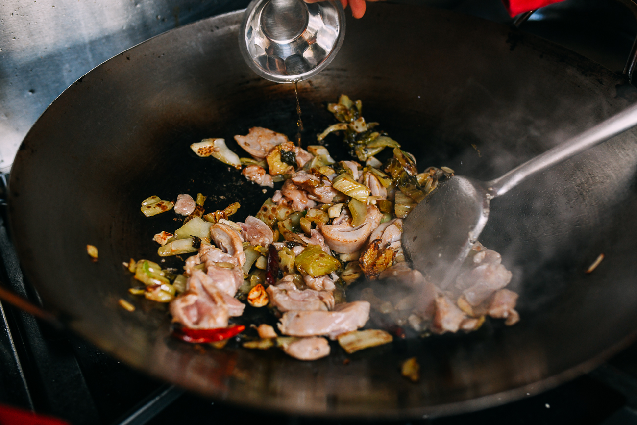 Adding Shaoxing wine to chicken and mustard greens in wok