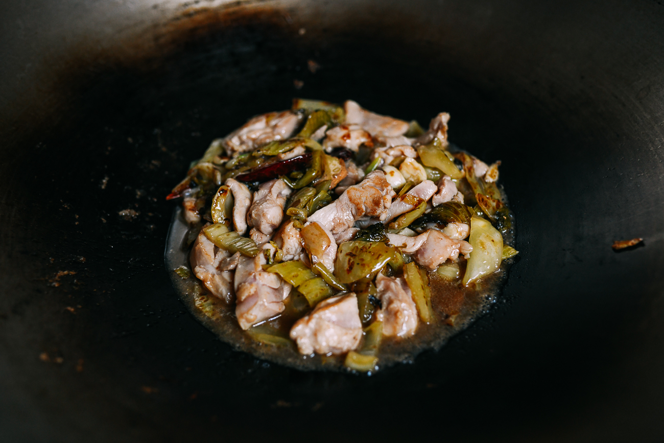 Chicken and mustard greens piled in center of the wok