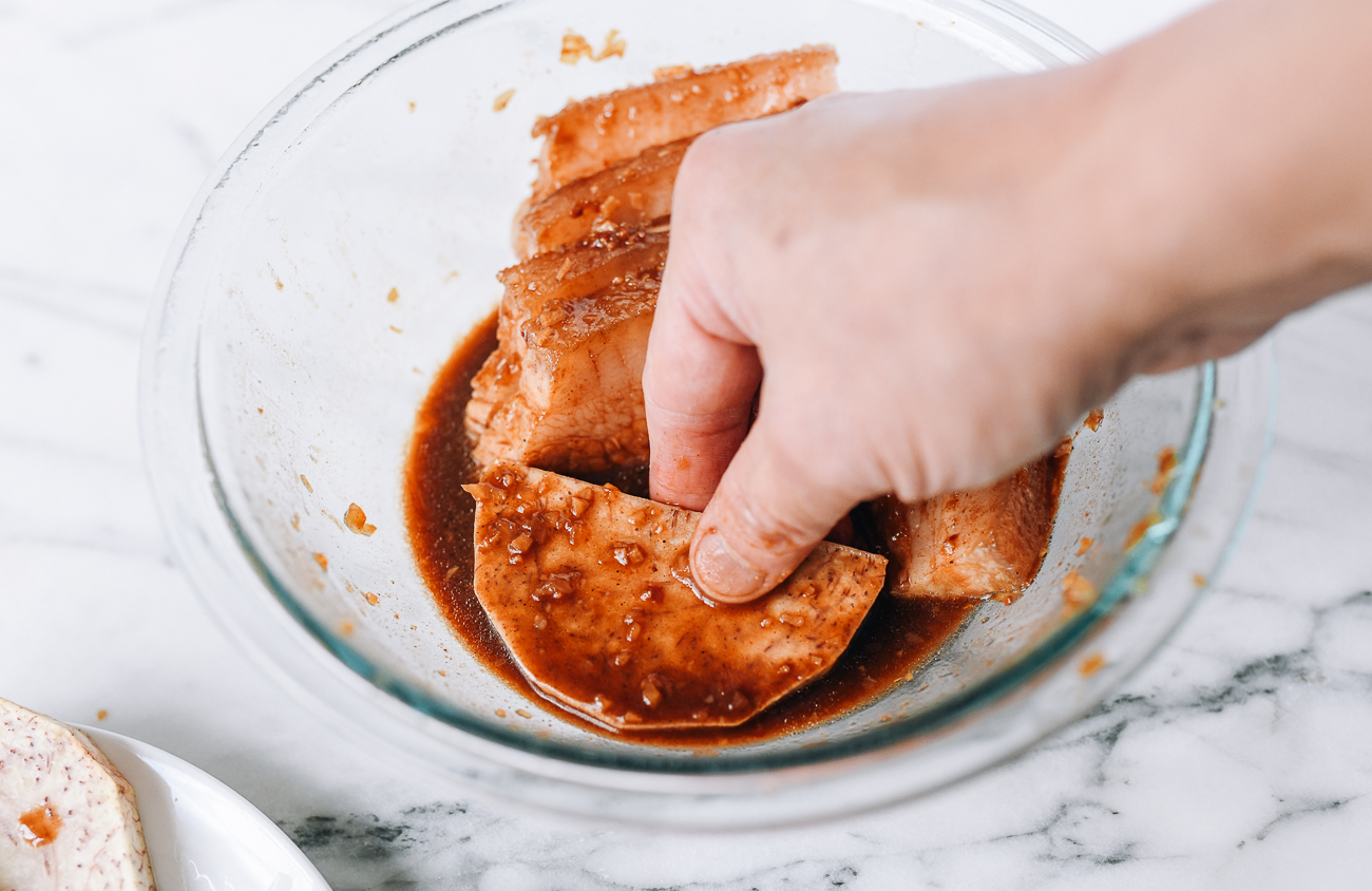 Dipping taro slice into marinade sauce