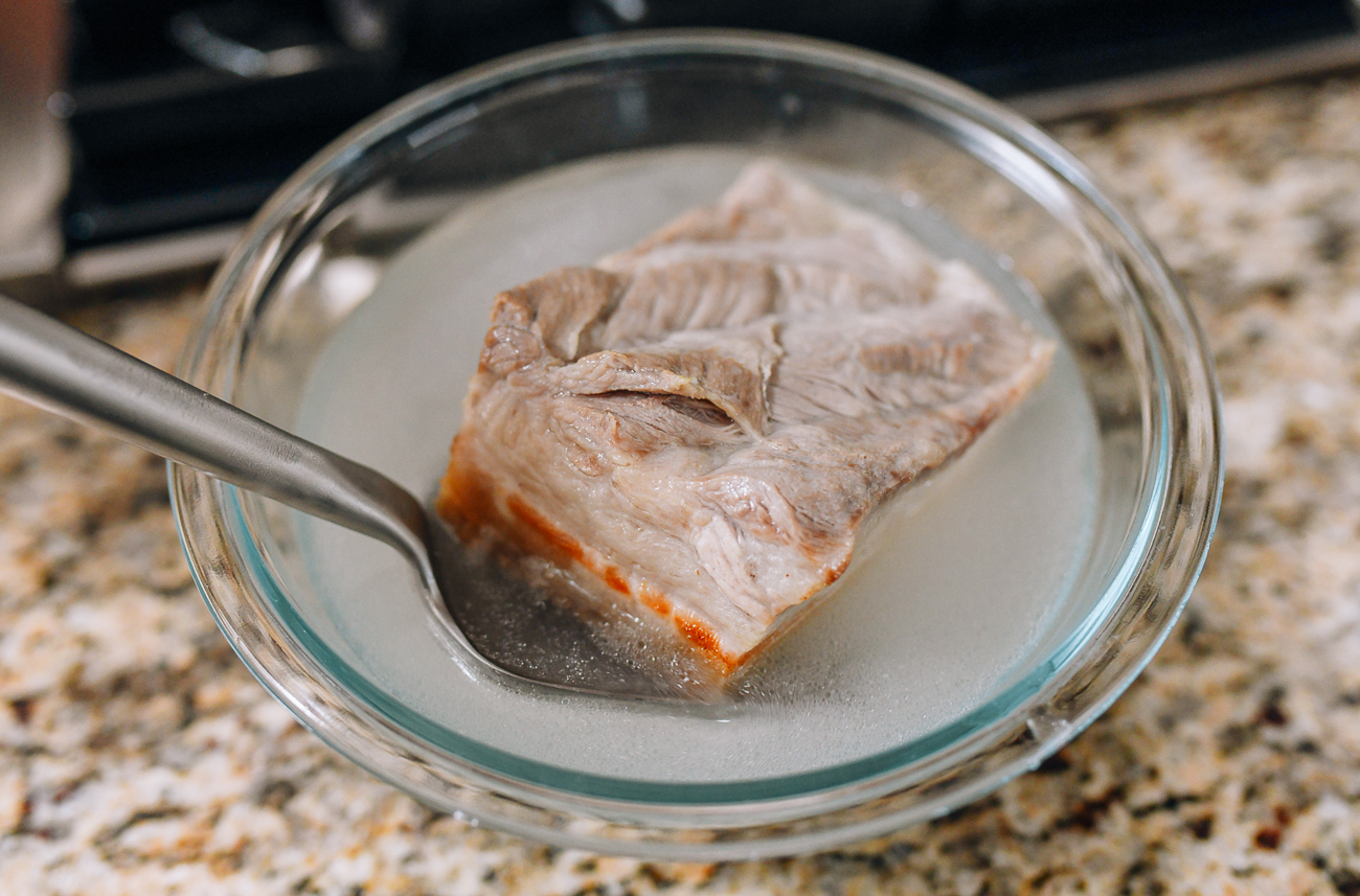 Putting fried pork belly into cooled blanching liquid