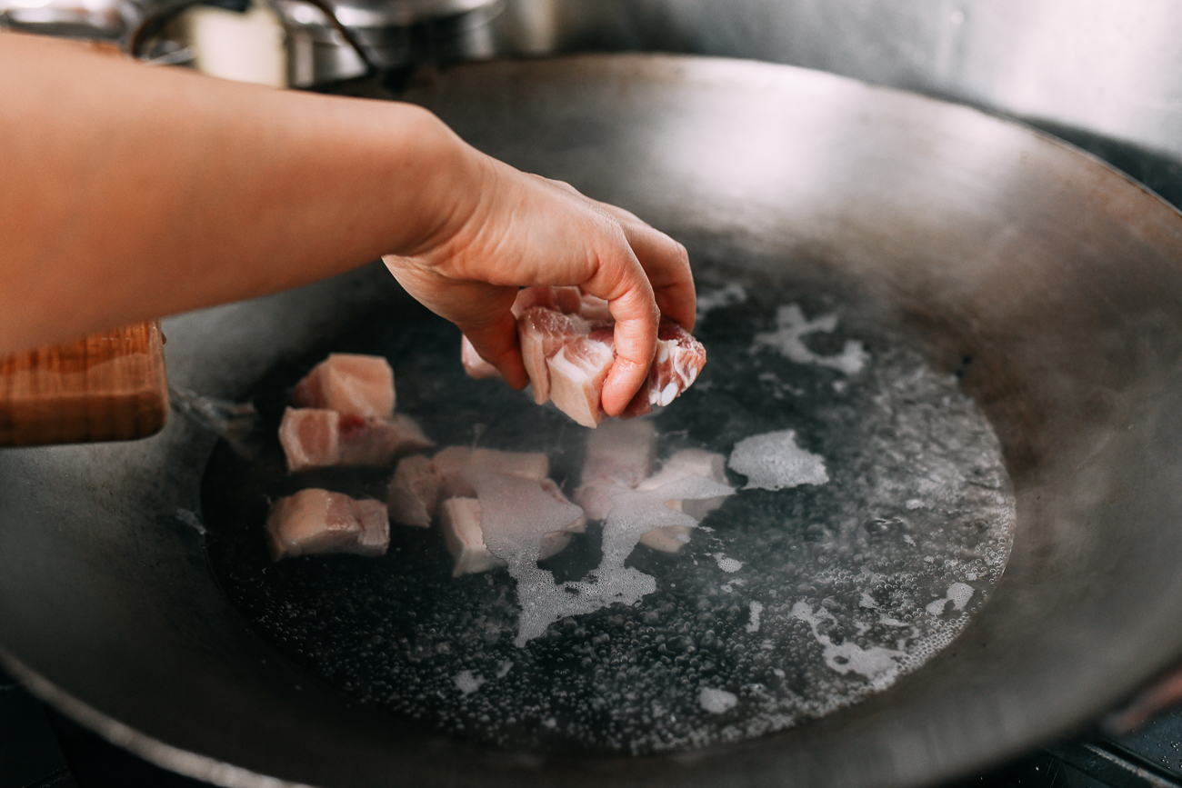 Adding pork belly to wok filled with water