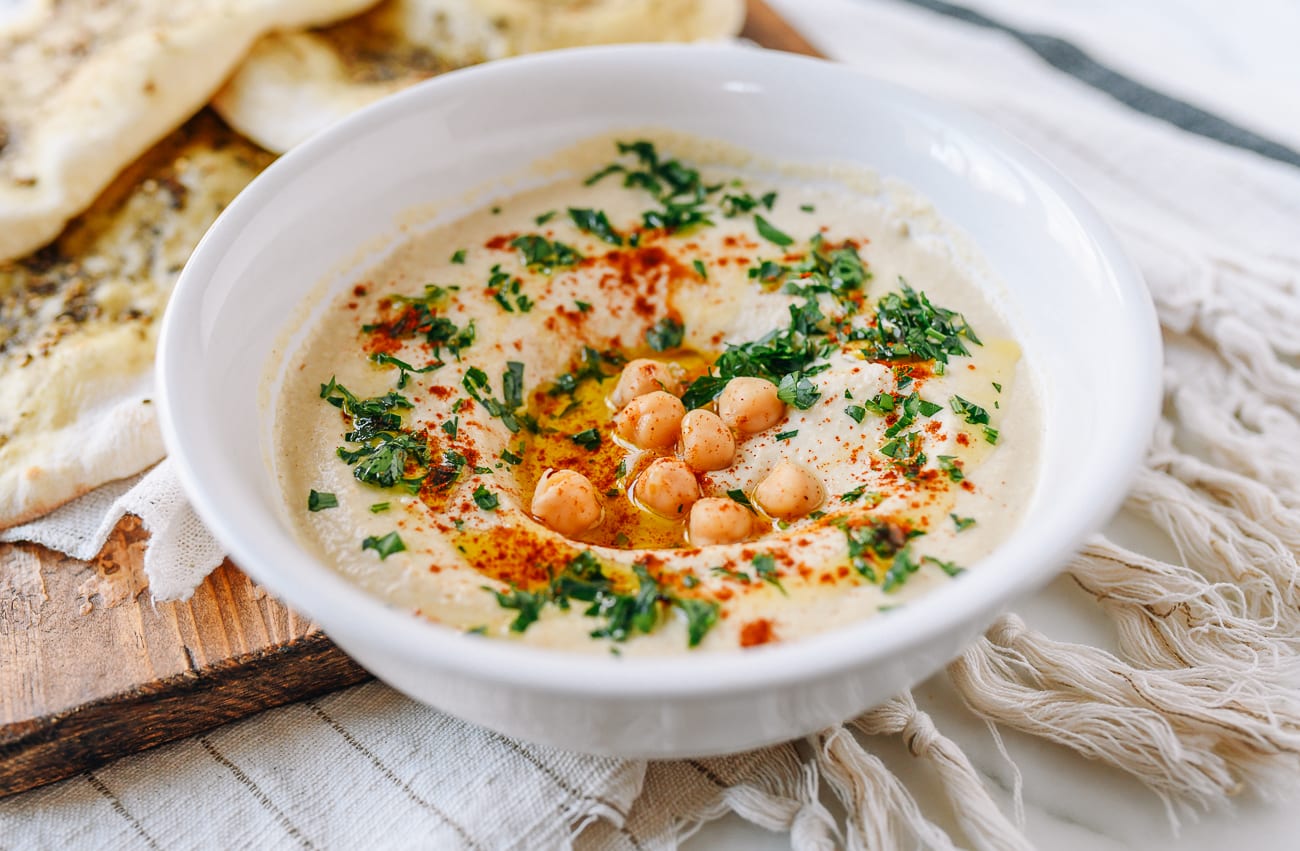 Hummus in white dish garnished with paprika, chickpeas, and parsley