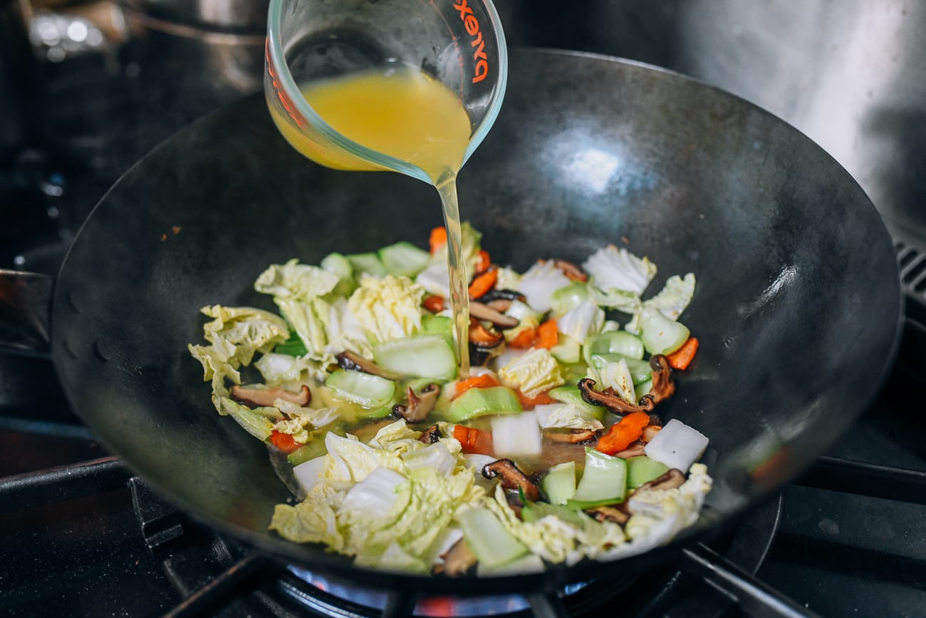 Pouring chicken stock into wok with vegetables