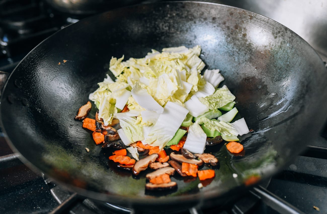 Adding napa cabbage to vegetables in wok