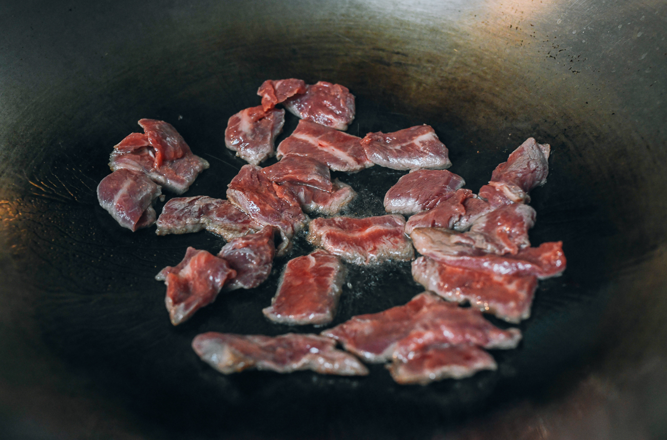 Adding sliced beef to wok in a single layer