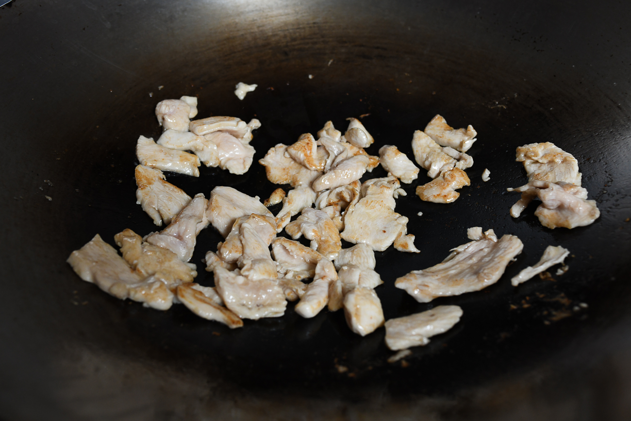 Stir-frying sliced chicken in wok