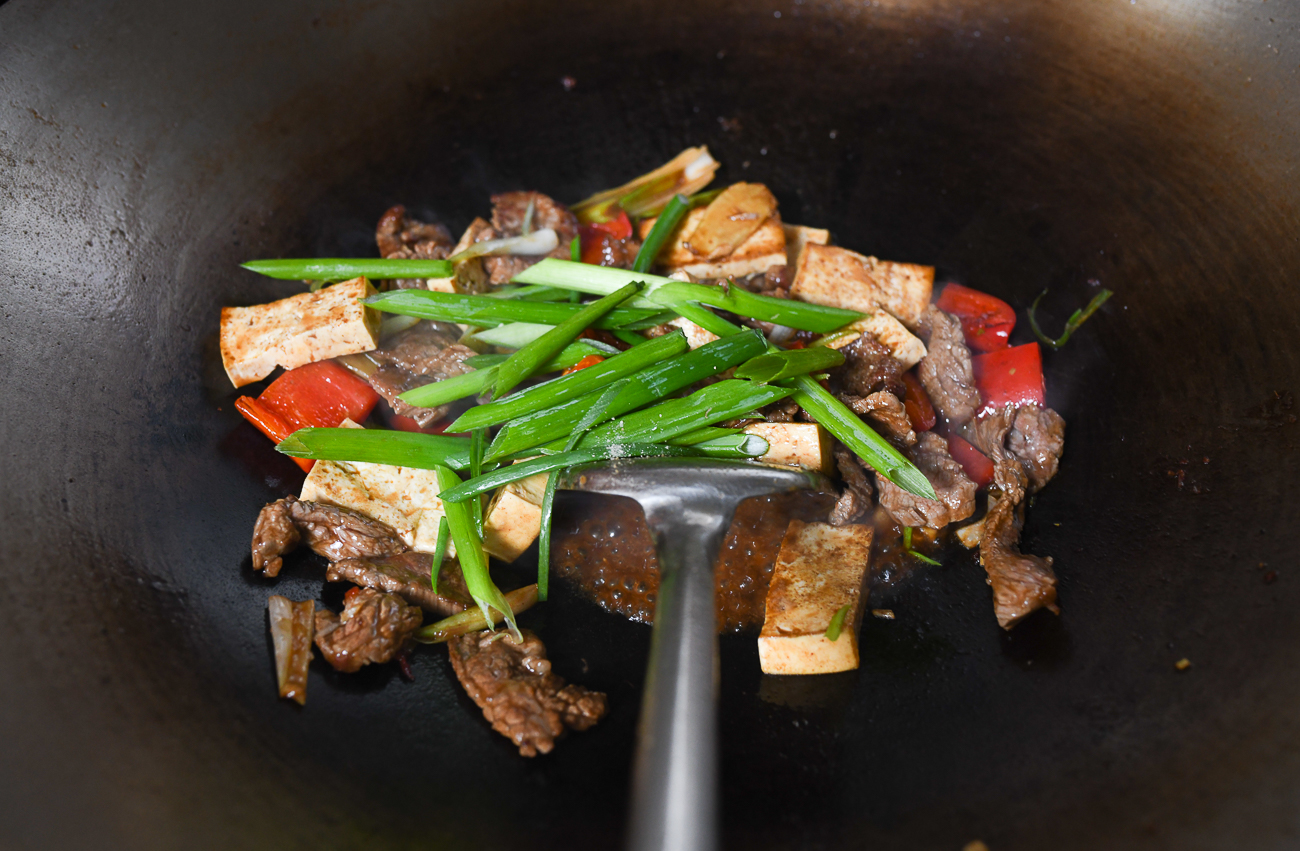 Adding scallions to beef and tofu stir-fry