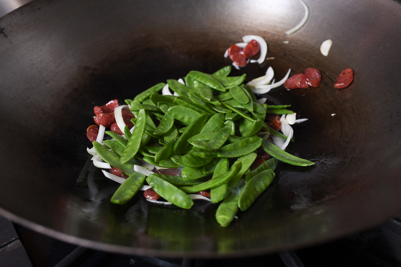 Adding snow peas to wok with onions and lap cheong
