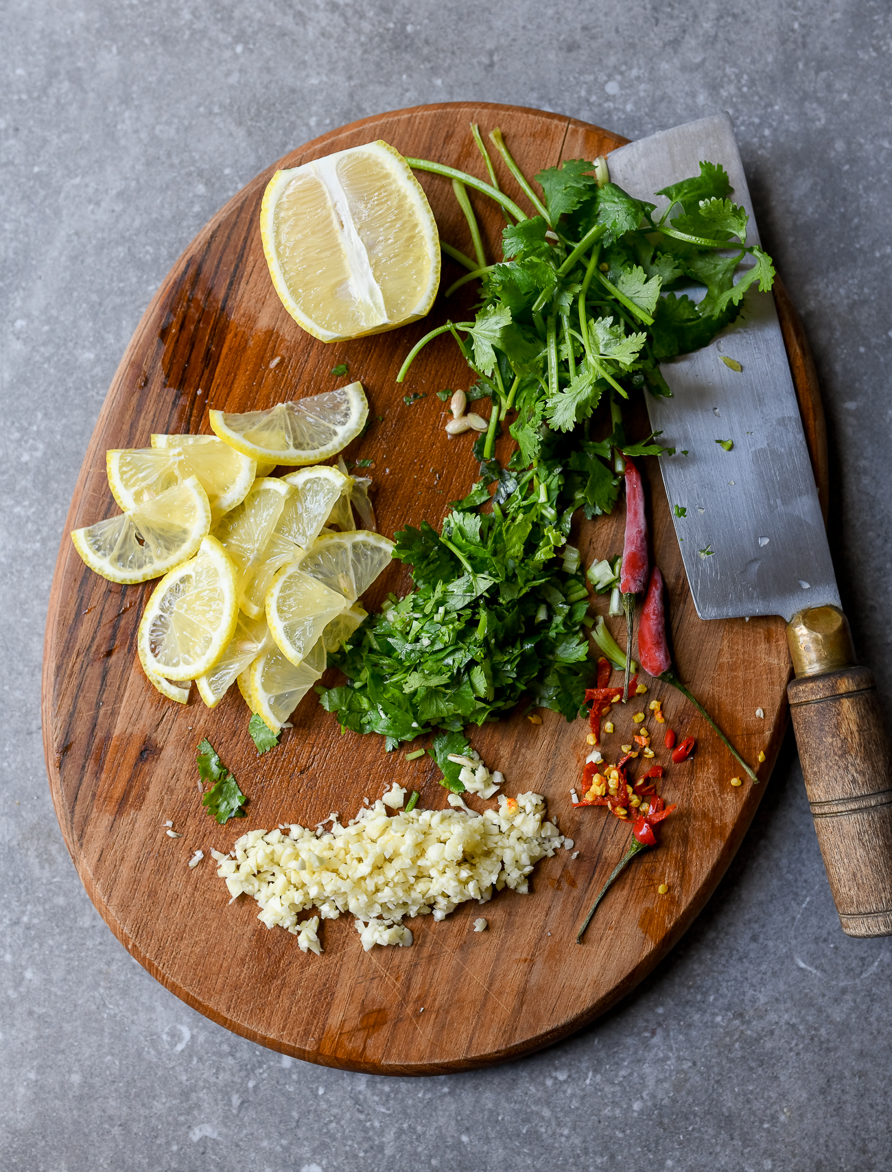Cutting board with garlic, lemon slices, cilantro, and chili