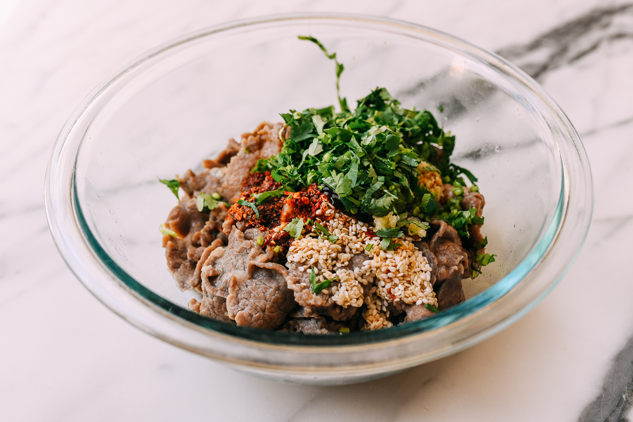 Beef, cilantro, chili, sesame seeds, in glass bowl