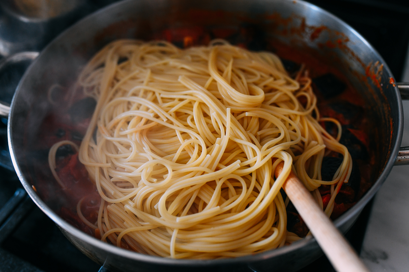 Adding spaghetti to sauce in pan