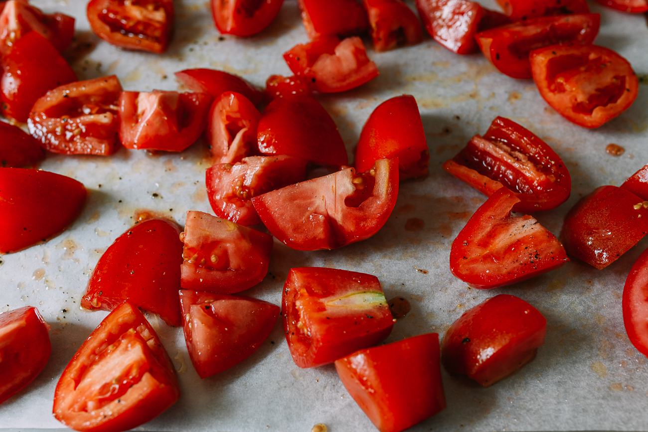 Chunks of tomato on baking sheet with olive oil, salt, and pepper