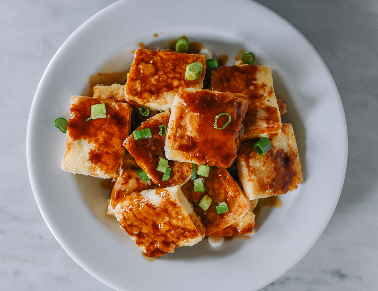 Crispy Tofu with sauce drizzled over the top and scallions