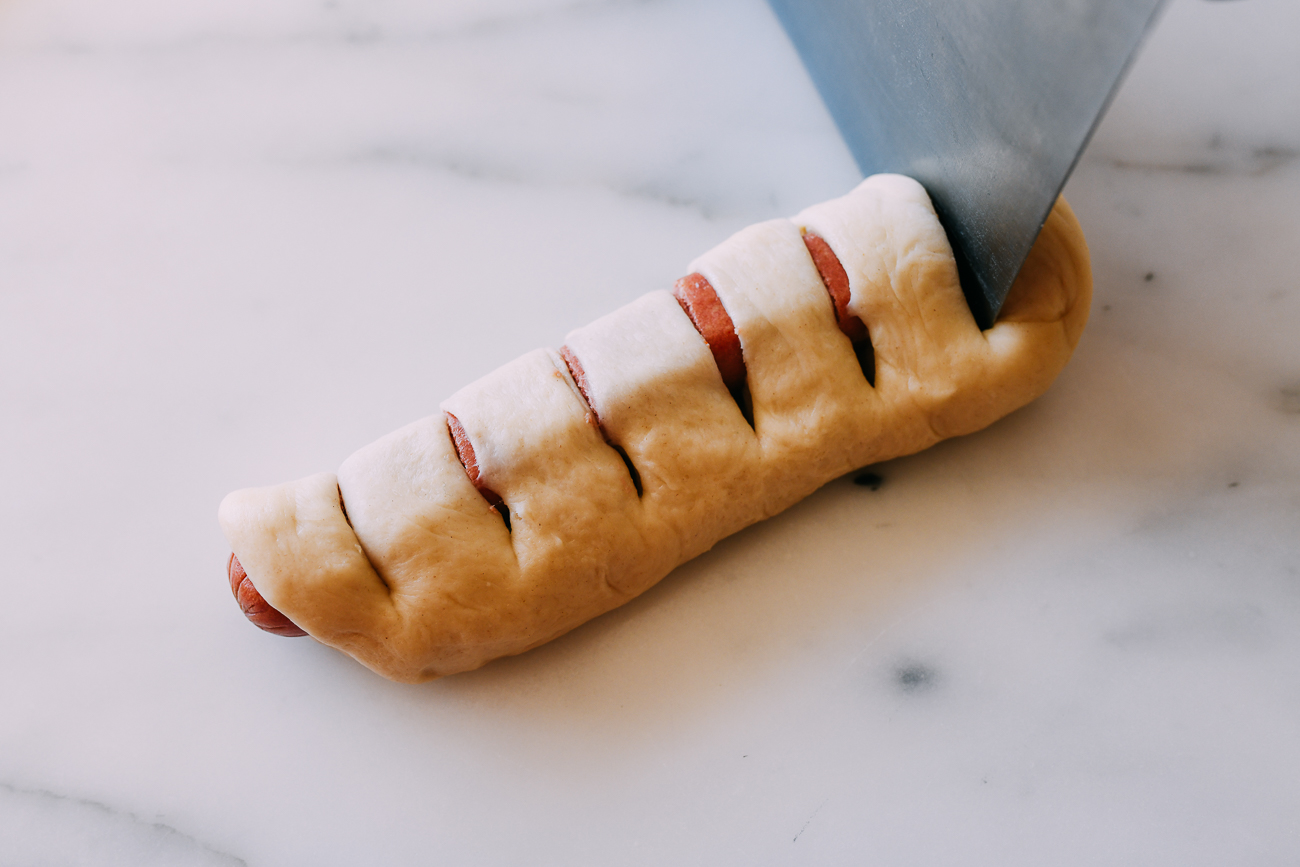 Cutting slits into dough with hot dog inside