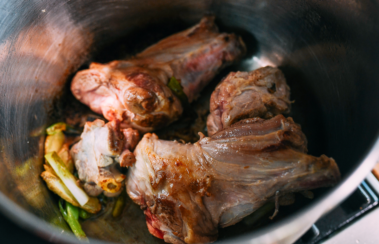 Browned lamb shanks in pot with ginger and scallions