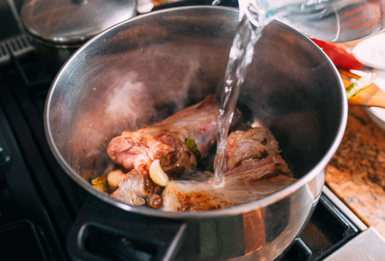 Pouring water over lamb shanks in pot