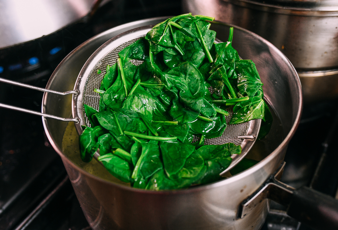 pulling blanched spinach out of pot with strainer