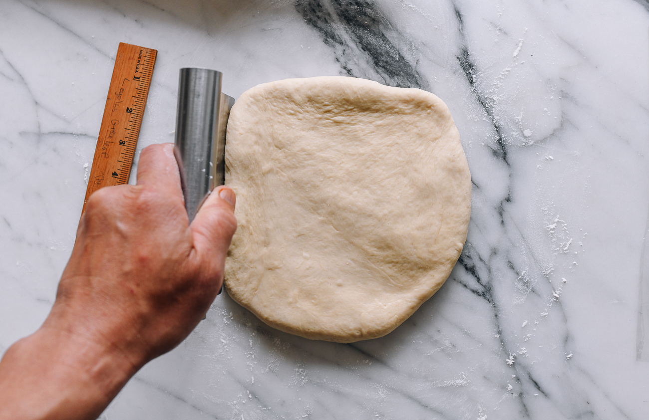 Using a bench scraper to sharpen the sides of a dough square