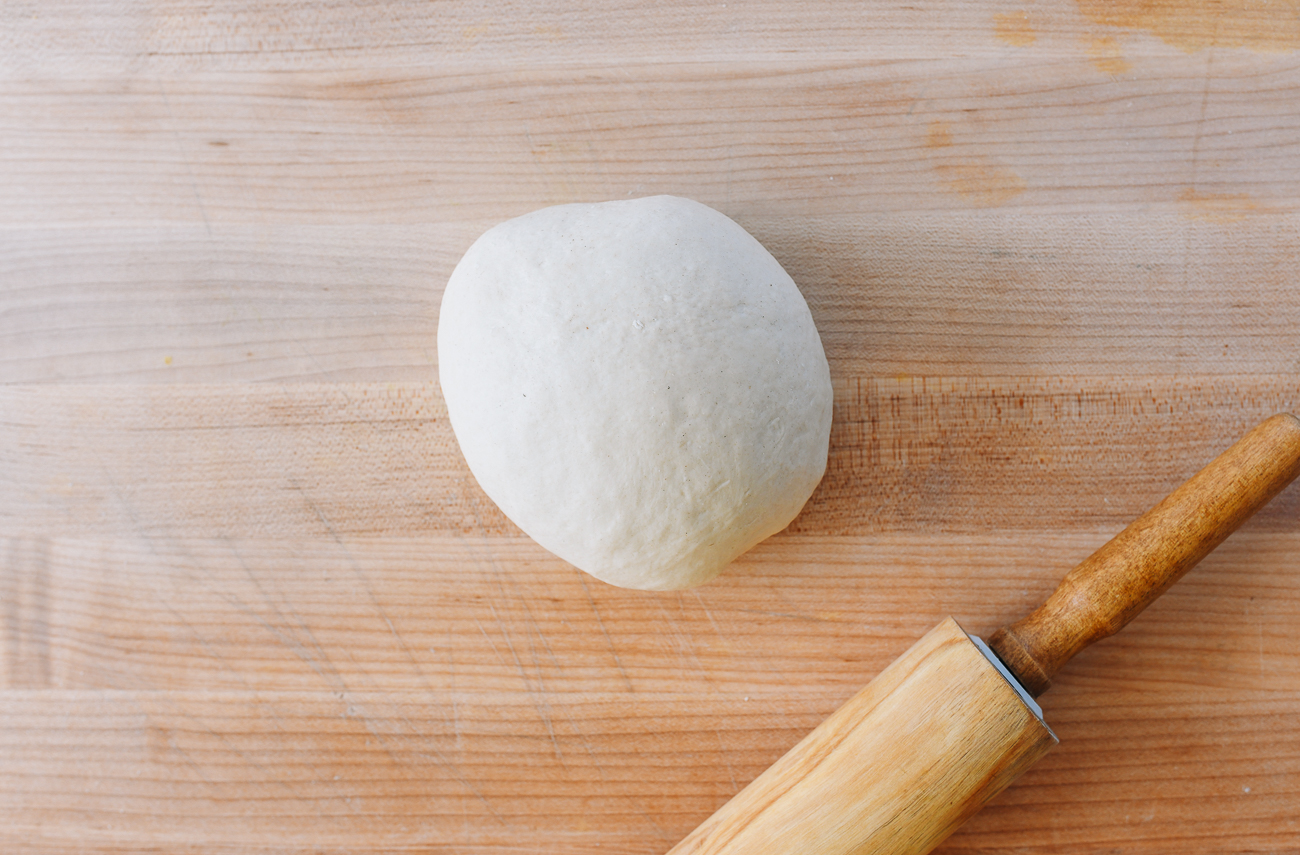 Dough ball on cutting board with rolling pin