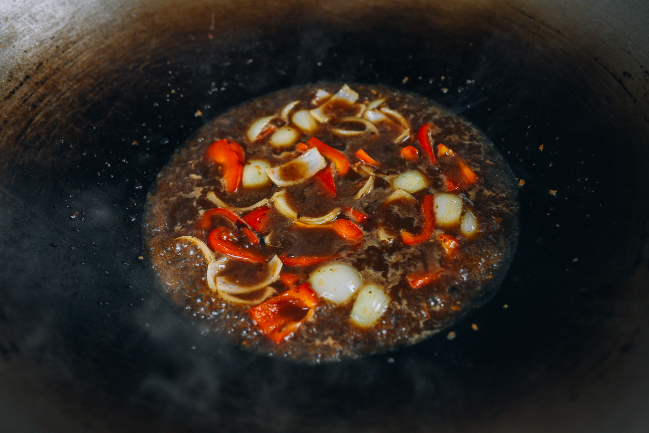 sauce mixture in wok with onions and peppers