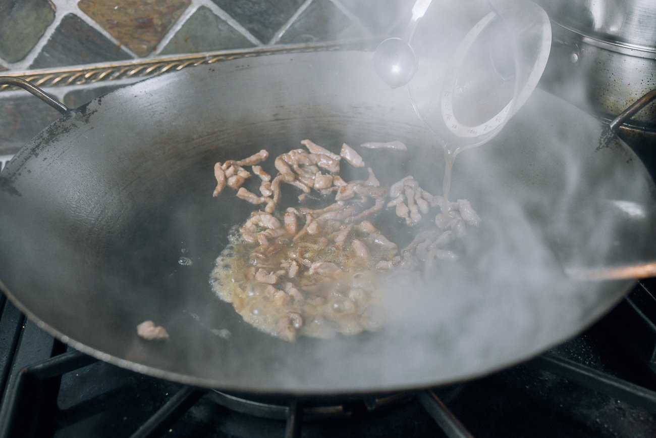 adding sauce to pork in wok