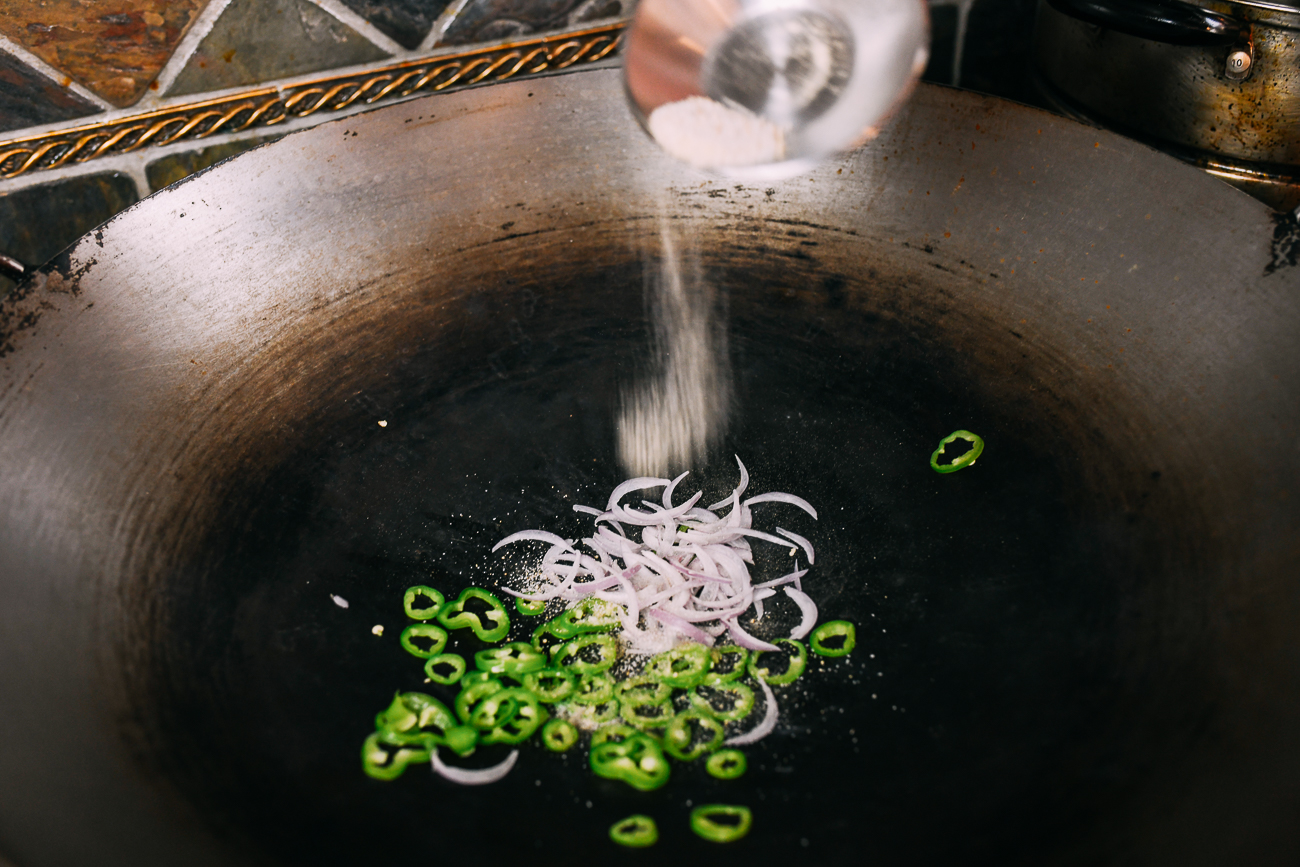 adding seasoned salt to peppers and shallots in wok