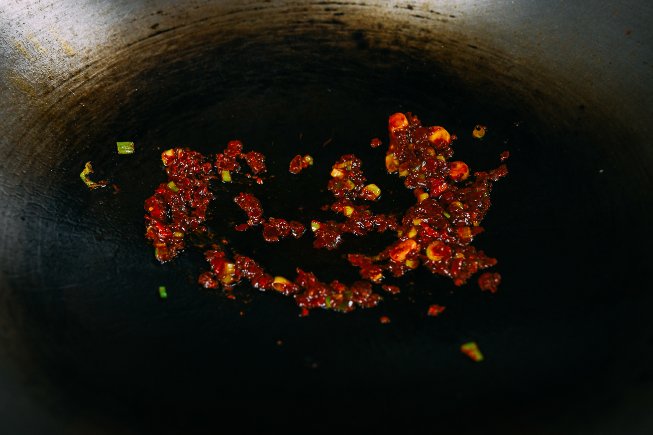 spicy bean sauce, tomato paste, and scallion whites in wok